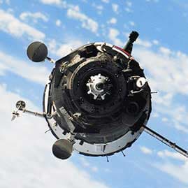 Nave espacial en órbita terrestre con paneles solares desplegados, sobre fondo de cielo y nubes